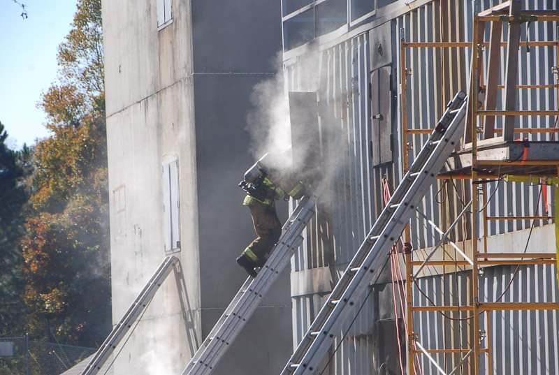 Firefighter climbing a ladder towards a smoky window to perform a Vent Enter Search During a Live Burn