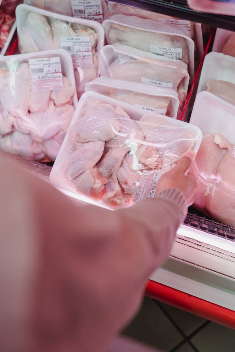 A shopper selects packaged chicken from a grocery store meat section.