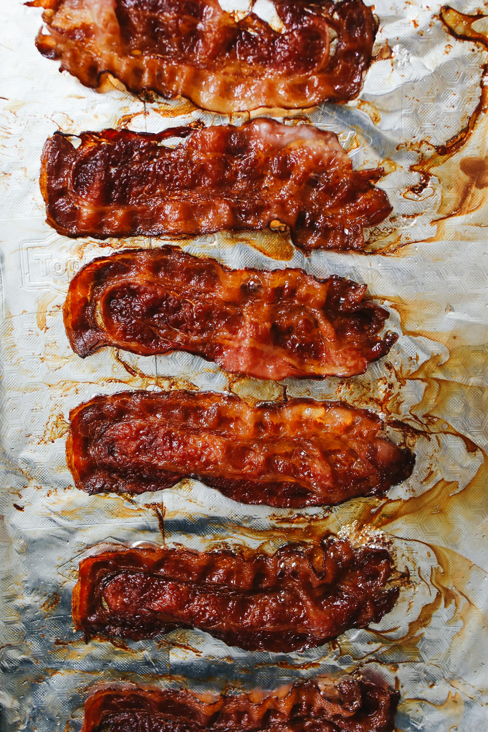 Crispy baked bacon strips freshly cooked on aluminum foil.