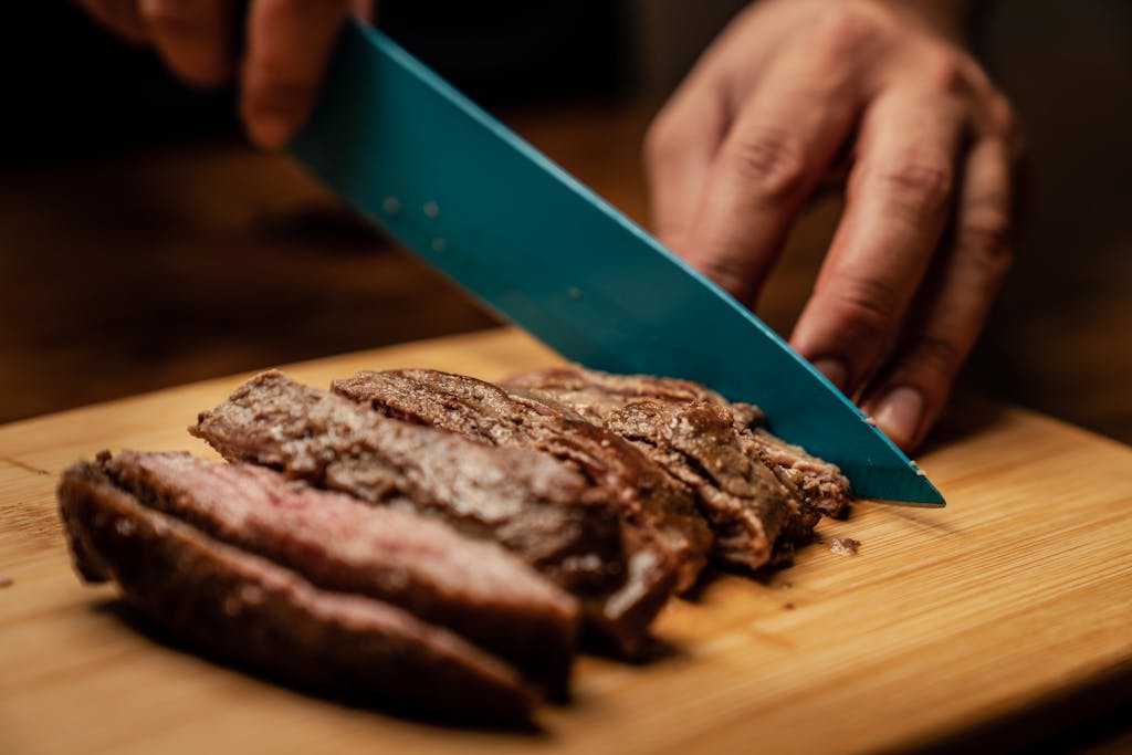 Hands slicing tender, juicy grilled steak on a wooden board, showcasing a mouth-watering culinary scene.